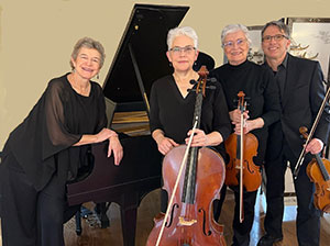 four people - one leaning on a piano and the other three with string instruments